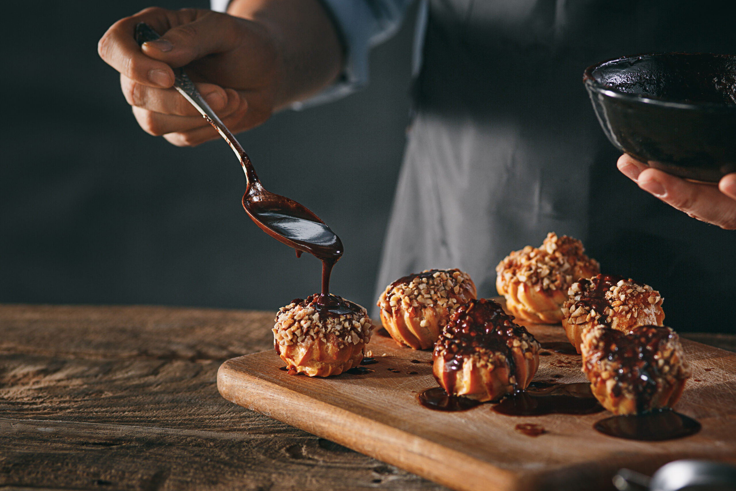 The male hands decorating delicious homemade eclairs with chocolate and peanuts